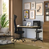 Moderní domácí pracovna s černou ergonomickou židlí GRÖNFJÄLL, dřevěným psacím stolem a nástěnnými obrazy.