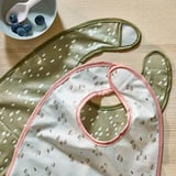 Květinové a puntíkované dětské bryndáčky na dřevěném stole, uvnitř měkké, zvenčí voděodolné.