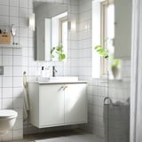 Moderní bílá koupelna s umyvadlem HAVBÄCK, umyvadlem, zrcadlem a rostlinami. Obklady a čisté dekory.