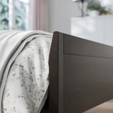 Moderní ložnice s postelí z tmavého dřeva, bílým květinovým povlečením, tlumeným osvětlením.