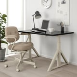 Černý nastavitelný psací stůl ikea IDÅSEN s bílou základnou, v kombinaci s béžovou otočnou židlí.