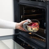 Osoba vkládá skleněnou mísu s bobulovým dezertem do trouby. Výrobek: IKEA 365+, vhodná do trouby a odolná pro ohřev jídla.