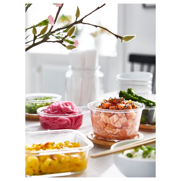Nádoby na potraviny s různými jídly, včetně sushi a kukuřice, aranžmá nádobí na stole, zdobené květinovými větvemi.