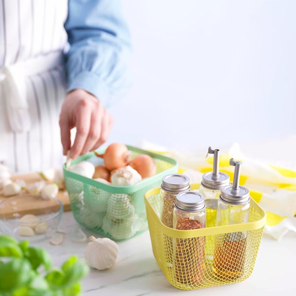 Osoba organizující čerstvé potraviny v zelených a žlutých síťových úložných koších IKEA 365+.