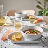 Jídelní stůl s bílou miskou polévky, toastů, sklenice a ubrousku IKEA 365+.