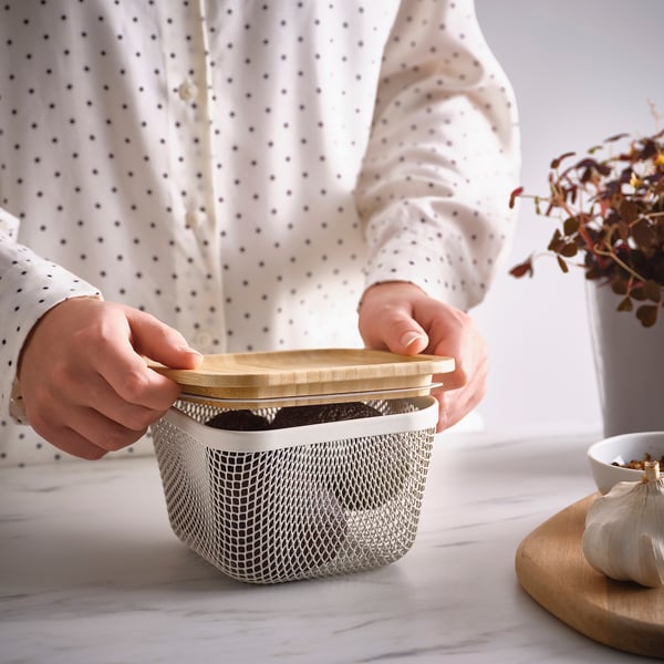 Osoba držící síťovaný košík na potraviny IKEA 365+ s víkem, který ukazuje skladování potravin a viditelnost.