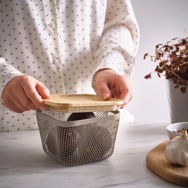 Osoba otevře na kuchyňské lince síťovaný košík na potraviny IKEA 365+ s dřevěným víkem.