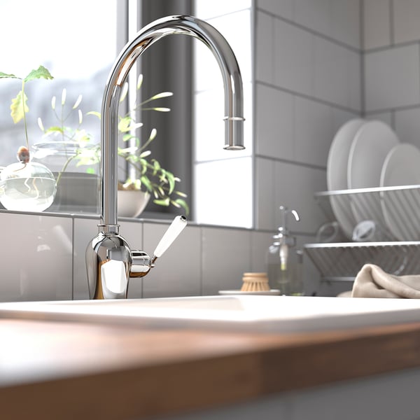 Moderní kuchyňská scéna s chromovou baterií INSJÖN, elegantní křivky, zobrazené na dlážděné stěně, obklopené zelení a nádobím.