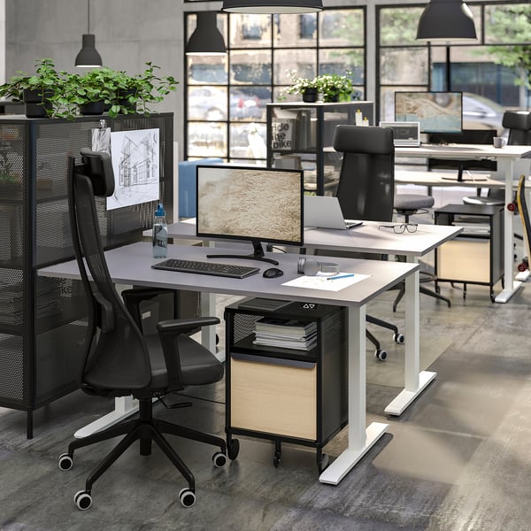 Moderní kancelář s ergonomickými stoly, dvěma monitory, rostlinami, velkými okny.