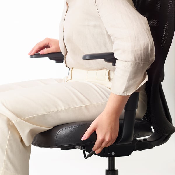 Osoba nastavující bederní opěrku na ergonomické kancelářské židli.