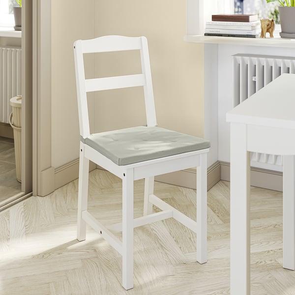 Bílá dřevěná židle s šedým polstrovaným sedákem, jednoduchý design, umístěná v útulné místnosti.