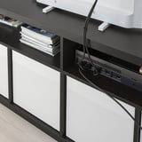 Černý televizní stolek KALLAX s bílými zásuvkami, zobrazující uspořádané kabely a usb rozbočovač, navržený pro snadné vedení kabelů.