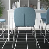 Tři světle modré židle s chromovanými nohami kolem bílého stolu na kostkované podlaze, s rostlinami a dekoracemi.