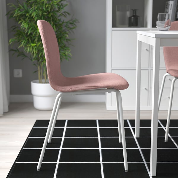 Moderní růžová židle s bílým rámem stojí na černobílém kostkovaném koberci v minimalistické místnosti.