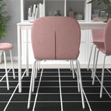 Tři růžové židle s bílými kovovými nohami kolem bílého stolu na černobílé dlážděné podlaze.