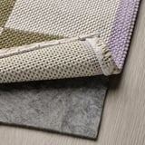 Barevný koberec s tkaným vzorem a plstěným podkladem spočívá na dřevěné podlaze.