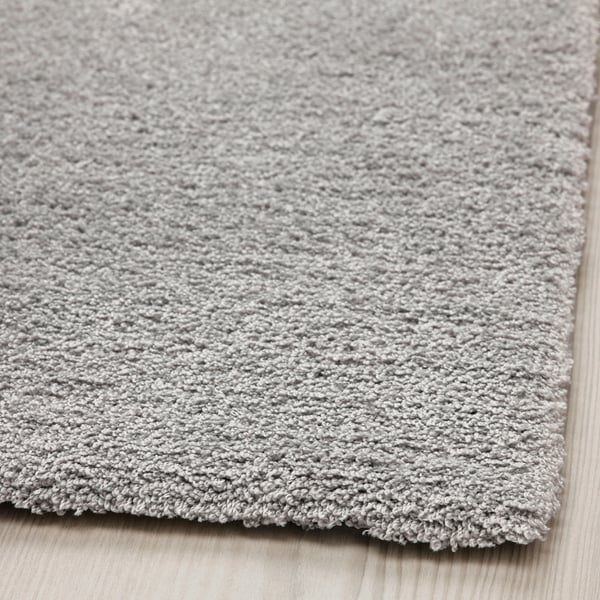Měkký, plyšový, světle šedý koberec s mírným leskem, položený na dřevěné podlaze. Silný, útulný, recyklovaný polyester.