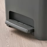 Moderní šedý koš částečně vytažený na dřevěné podlaze.