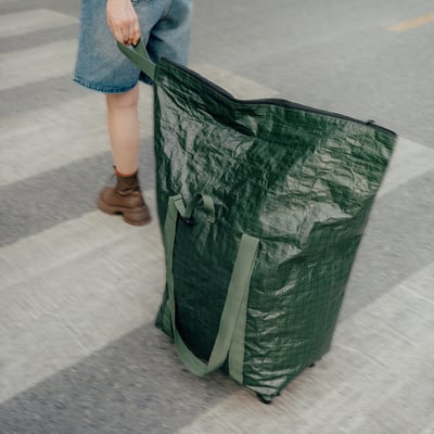 Osoba s velkou zelenou taškou Kompishang na kolečkách, džíny, botách.