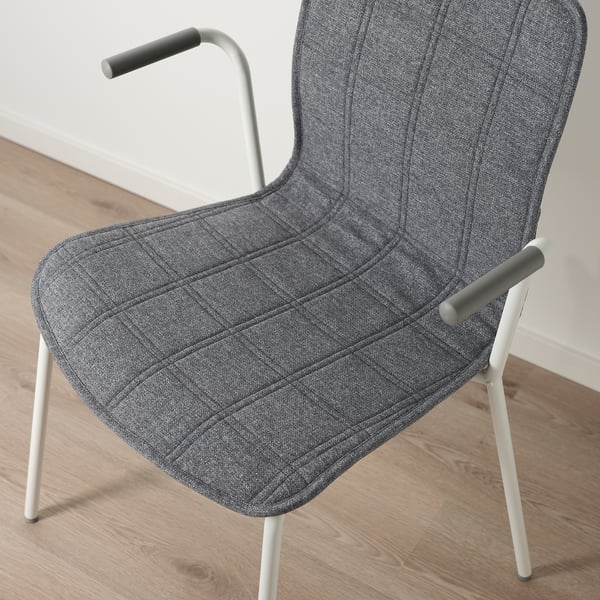 Moderní židle s šedou látkou, bílými nohami, zakřivenými područkami, posazená na dřevěné podlaze.