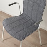 Moderní židle s šedou látkou, bílými nohami, zakřivenými područkami, posazená na dřevěné podlaze.