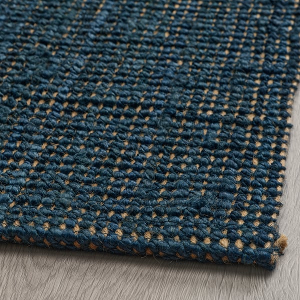 Texturovaný tmavě modrý jutový koberec, hladce tkaný, vystavený na dřevěné podlaze.
