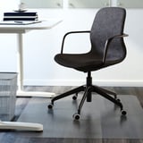 Moderní černá kancelářská židle s područkami a kolečky pod bílou deskou na skleněné podložce.