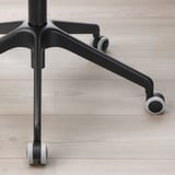 Detailní záběr na černou základnu kancelářské židle s robustními područkami a hladkými kolečky, která představuje odolný design a materiály.