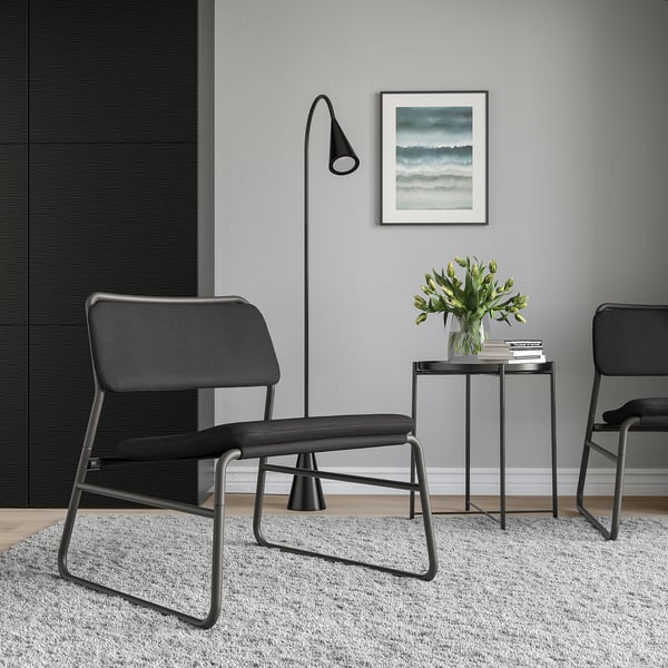 Minimalistický obývací prostor s černými židlemi LINNEBÄCK, moderním odkládacím stolkem, elegantní lampou a květinovou vázou. Umělecká díla na stěně. Útulný, moderní dekor.