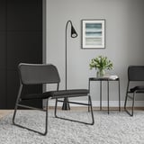 Minimalistický obývací prostor s černými židlemi LINNEBÄCK, moderním odkládacím stolkem, elegantní lampou a květinovou vázou. Umělecká díla na stěně. Útulný, moderní dekor.