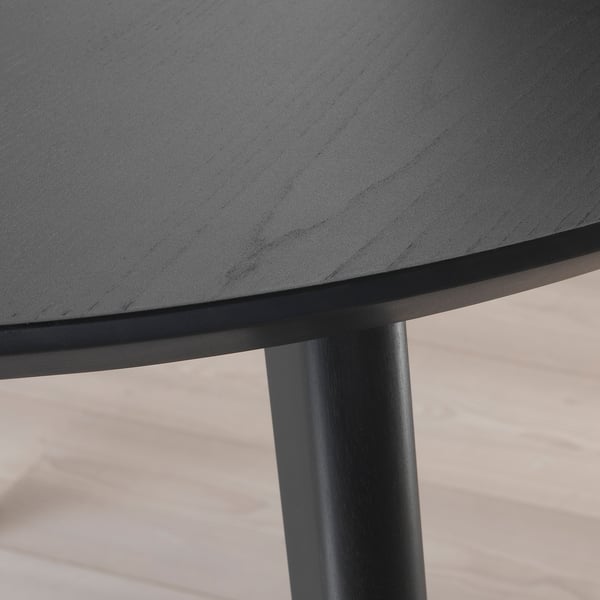 Detailní záběr na černý kulatý okraj stolu s hladkým povrchem a robustní nohou, zdůrazňující kvalitní řemeslné zpracování.