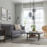 Moderní obývací pokoj s šedým konferenčním stolkem LISTERBY, elegantními liniemi, vrchní deskou z bukové dýhy. Závěsná světla, pruhovaný koberec, pohovka a výhled na balkon.