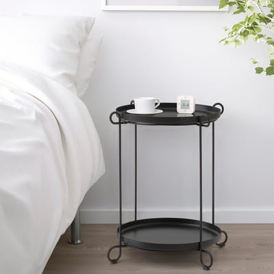 Černý odkládací stolek s podnosy v minimalistické ložnici, držící šálek a gadget.