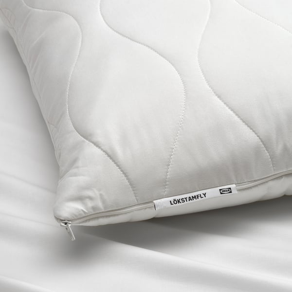 Detail bílého ergonomického polštáře se složitým prošíváním, na kterém je cedulka s nápisem LÖKSTAMFLY by ikea.