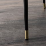 Detail černé nohy stolu se zlatou špičkou na dřevěné podlaze.