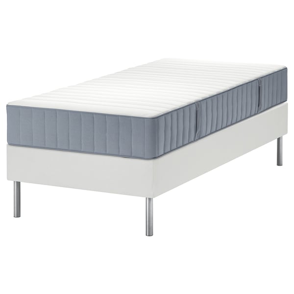 Bílá postel LYNGÖR s matrací valevåg. Postel má minimalistický design s kovovými nohami a plochým, rovným povrchem pro podporu.