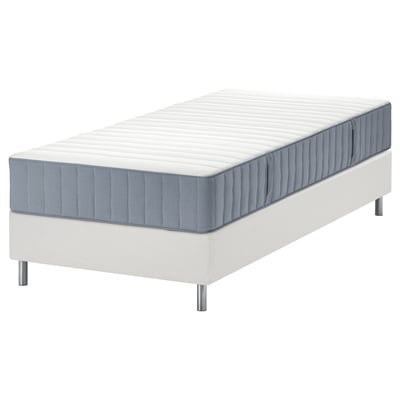 Moderní, bílá postel s modrošedou matrací, vyvýšená na nožičkách.