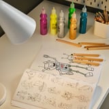 Barevný stůl s uměleckými potřebami a lampou osvětlující omalovánky robota.