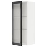 Vystavuje bílou kuchyňskou skříňku METOD s černými skleněnými dvířky hejsta s designem rákosového skla a elegantním kovovým rámem.