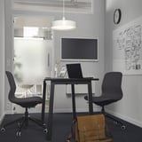 Moderní kancelář se stolem MITTZON, židlemi, notebookem, taškou, tabulí, plochou obrazovkou. Světlé, minimalistické.