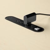 Černá oválná zásuvka na stole s několika USB porty a černým krychlovým konektorem na světlé dřevěné desce.