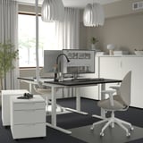 Moderní čistá kancelář: Bílý výškově nastavitelný stůl MITTZON, šedá židle, elegantní design, monitor a úložné jednotky.