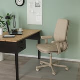 Domácí kancelář: židle ikea MULLFJÄLLET, stůl s lampou, notebook, hrnek; zelené stěny s výzdobou.