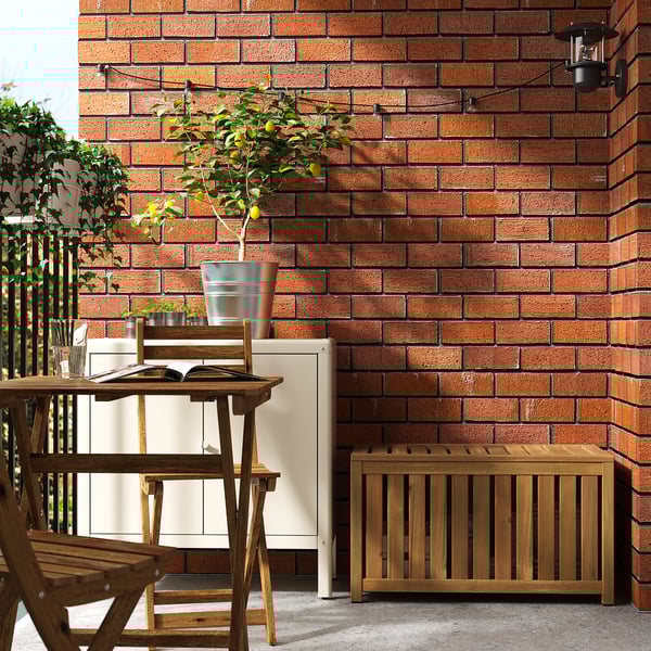 Balkon se zdí z červených cihel, dřevěným nábytkem, citroníkem a úložným boxem. Malá, úhledná sestava.