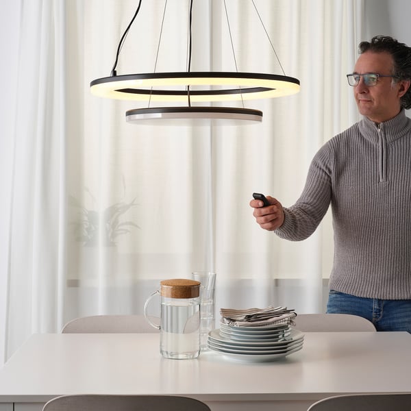 Muž nastavovací moderní závěsná lampa s dálkovým ovládáním, ovládající jas nad elegantním nastavením jídelního stolu.