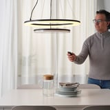 Muž nastavovací moderní závěsná lampa s dálkovým ovládáním, ovládající jas nad elegantním nastavením jídelního stolu.
