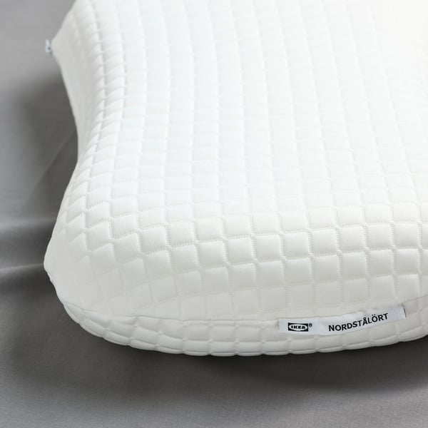 Detail bílého ergonomického polštáře IKEA pro spáče na zádech/boku, s texturovaným potahem a měkkou pěnou.