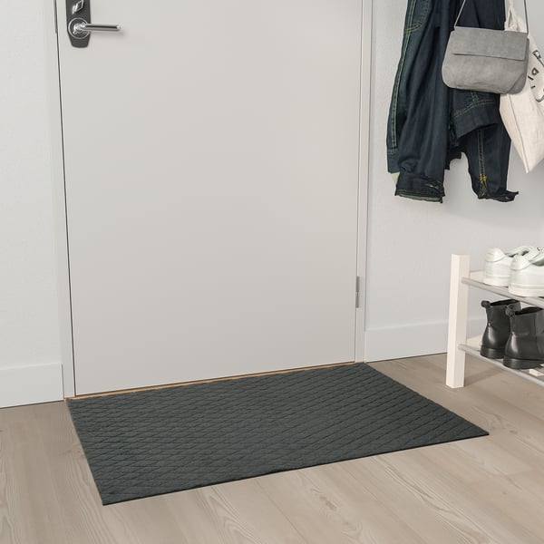 Šedá ÖSTERILD podložka u bílých dveří, recyklovaný polyester, textura.