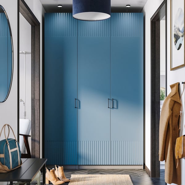 Místnosti dominuje moderní modrá šatní skříň PAX, vysoká s elegantním designem. Poblíž visí kabáty, dole tašky a boty, zrcadlové dveře odrážejí prostor.