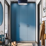 Místnosti dominuje moderní modrá šatní skříň PAX, vysoká s elegantním designem. Poblíž visí kabáty, dole tašky a boty, zrcadlové dveře odrážejí prostor.
